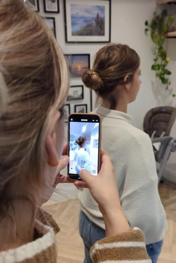 A helper filming a woman on a smartphone while she holds her pose