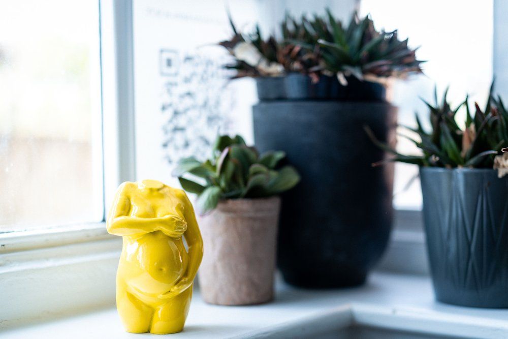Yellow pregnancy sculpture on a windowsill among plants